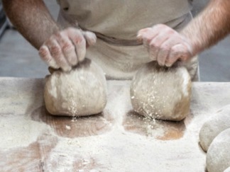 Hände kneten Brotteig auf Mehlfläche